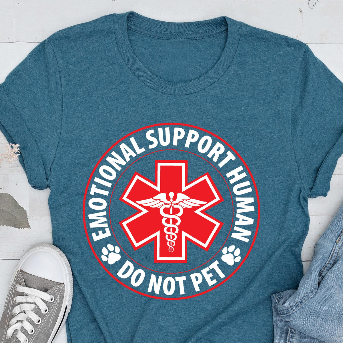 May include: Teal-colored t-shirt featuring a red and white graphic. The graphic includes a red star with a medical symbol, the words "EMOTIONAL SUPPORT HUMAN" and "DO NOT PET" in a circular design, and paw prints.