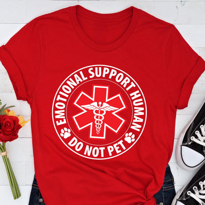 May include: A red t-shirt featuring a white graphic with the text "EMOTIONAL SUPPORT HUMAN DO NOT PET". The graphic includes a medical symbol with a caduceus in the center and paw prints.