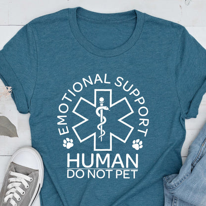 May include: A teal short-sleeved t-shirt featuring a white graphic of a six-pointed star of life symbol with a snake and staff. The text reads EMOTIONAL SUPPORT HUMAN DO NOT PET, accompanied by two small paw print icons on either side of the central emblem.