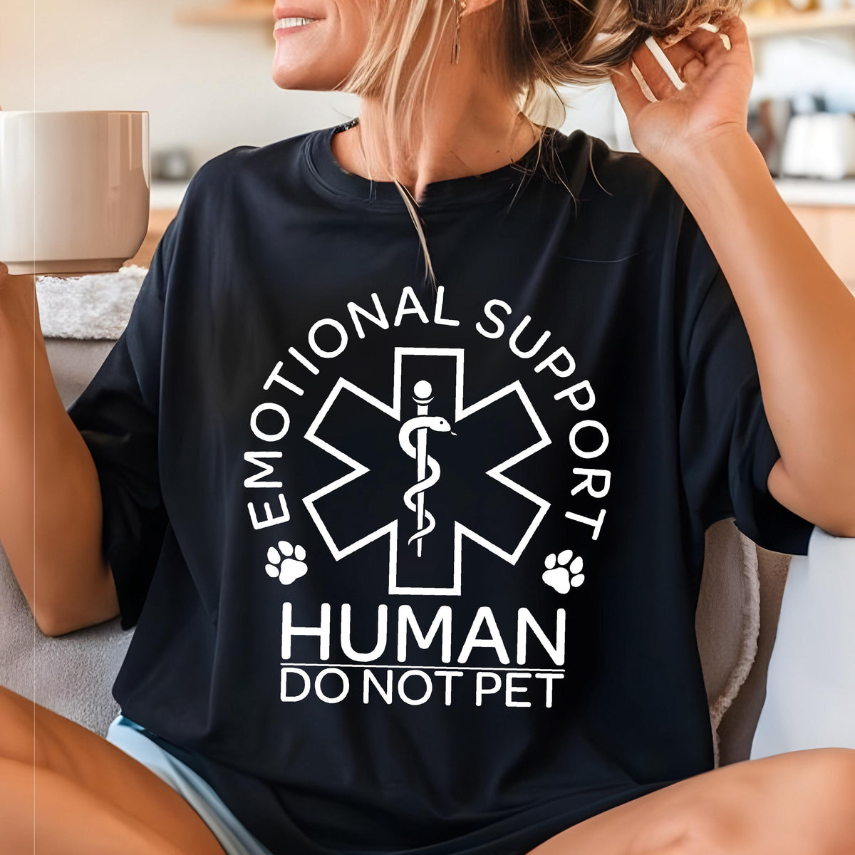 May include: A black t-shirt featuring a white graphic of a Star of Life symbol with a snake and staff, surrounded by the text "EMOTIONAL SUPPORT HUMAN DO NOT PET" and two small paw print icons positioned on either side of the central emblem.