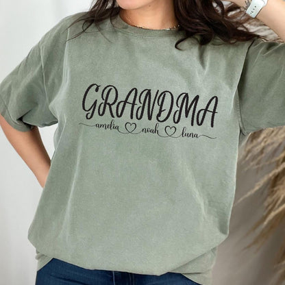 May include: Green t-shirt with the text "Grandma" and the names "Amelia", "Noah", and "Luna" written below in a cursive font.