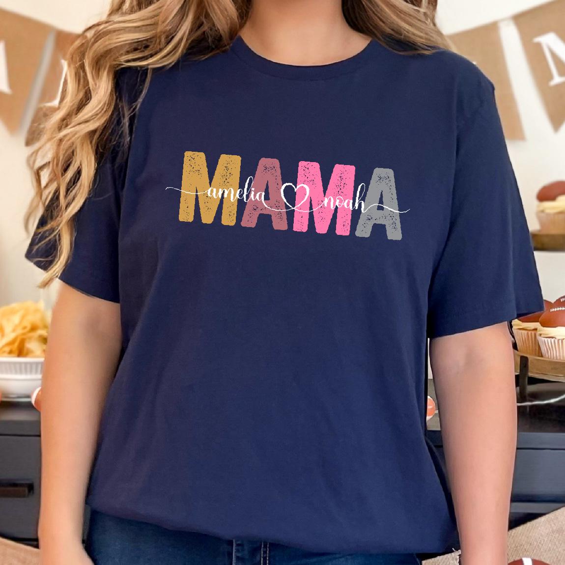 May include: A navy blue t-shirt with the word "MAMA" in colorful, distressed letters. The text "amelia & noah" is written in cursive below the word "MAMA".