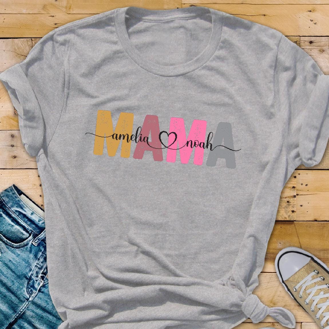 May include: Gray t-shirt with the word "MAMA" in colorful letters, with the names "Amelia" and "Noah" written in cursive on either side of the heart.