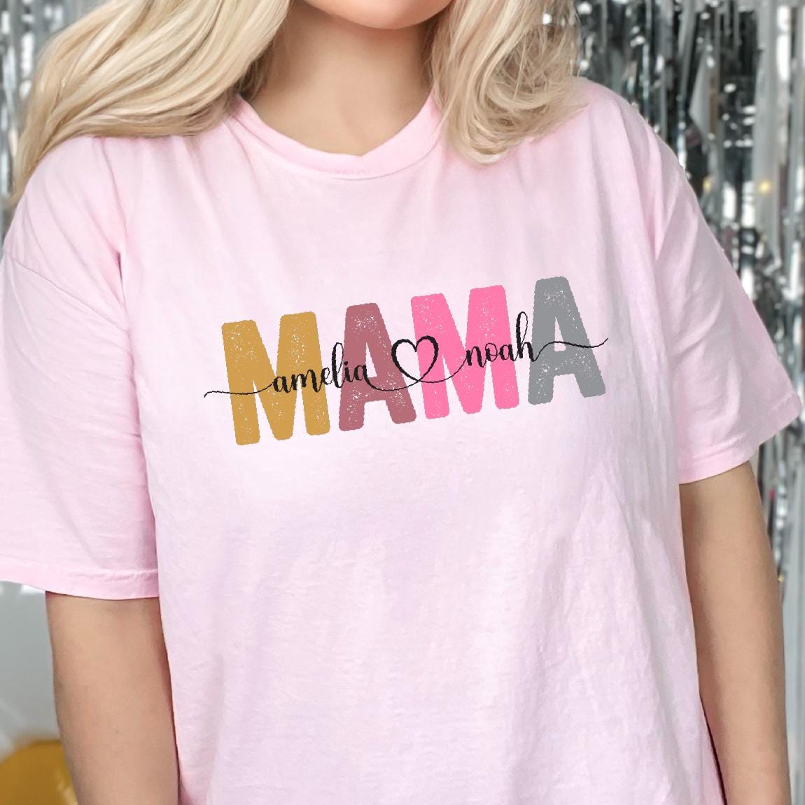 May include: Pink t-shirt with the word "MAMA" in colorful letters, with the names "Amelia" and "Noah" written in cursive on either side of the heart.