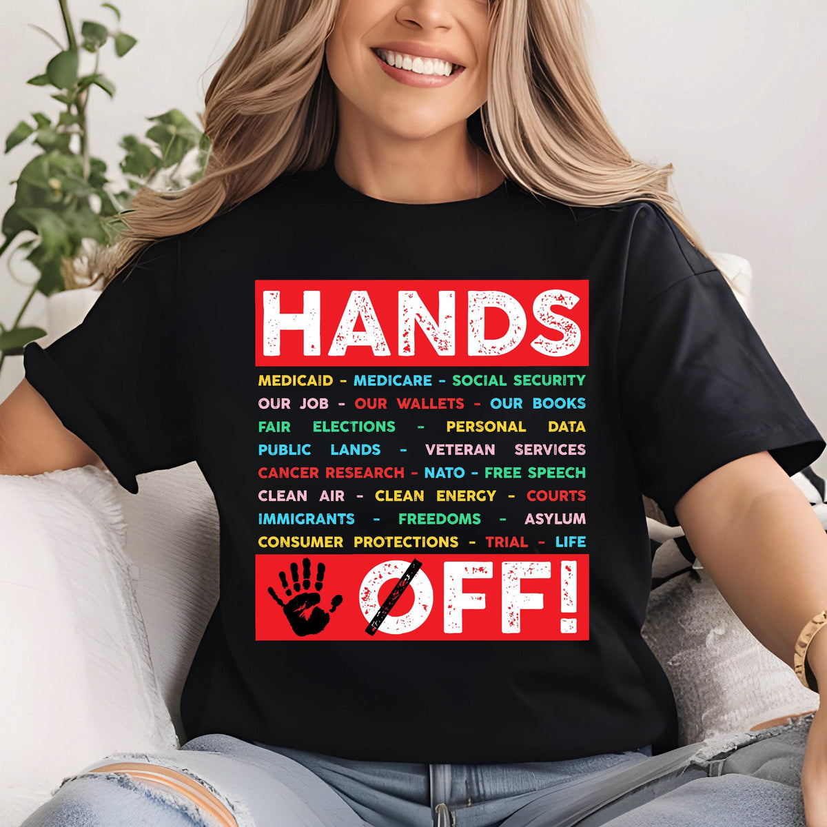 May include: Black t-shirt with the text "HANDS OFF!" in red. The text is surrounded by a list of items in different colors, including "Medicaid", "Medicare", "Social Security", "Our Job", "Our Wallets", "Our Books", "Fair Elections", "Personal Data", "Public Lands", "Veteran Services", "Cancer Research", "NATO", "Free Speech", "Clean Air", "Clean Energy", "Courts", "Immigrants", "Freedoms", "Asylum", "Consumer Protections", "Trial", and "Life". A red hand with a diagonal line through it is below the text.