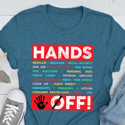 May include: A teal blue t-shirt with the text "HANDS OFF!" in red and white. The text is surrounded by a list of items in various colors, including "Medicaid", "Medicare", "Social Security", "Our Job", "Our Wallets", "Our Books", "Fair Elections", "Personal Data", "Public Lands", "Veteran Services", "Cancer Research", "NATO - Free Speech", "Clean Air", "Clean Energy", "Courts", "Immigrants", "Freedoms", "Asylum", "Life", and "Consumer Protections - Trial".