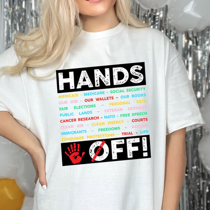 May include: White t-shirt with a black graphic that says "Hands Off!" with a list of items including Medicaid, Medicare, Social Security, our job, our wallets, our books, fair elections, personal data, public lands, veteran services, cancer research, NATO, free speech, clean air, clean energy, courts, immigrants, freedoms, asylum, consumer protections, trial, and life.