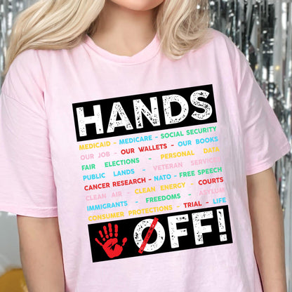 May include: Pink t-shirt with the text "HANDS OFF!" in black with a red handprint and a diagonal line through it. The text is surrounded by a list of items in various colors, including "Medicaid", "Medicare", "Social Security", "Our Job", "Our Wallets", "Our Books", "Fair Elections", "Personal Data", "Public Lands", "Veteran Service", "Cancer Research", "NATO", "Free Speech", "Clean Air", "Clean Energy", "Courts", "Immigrants", "Freedoms", "Asylum", "Consumer Protections", "Trial", and "Life".