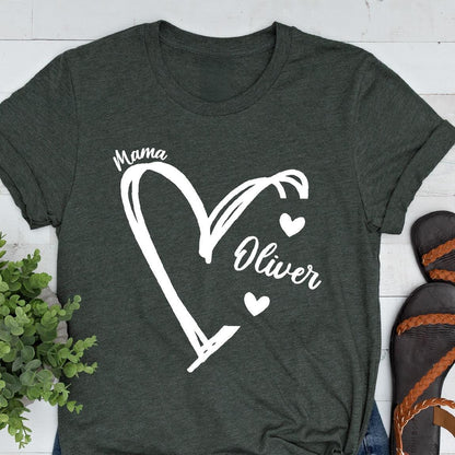 May include: A dark green t-shirt with a white heart design. The heart is divided into two sections, one labeled "Mama" and the other labeled "Oliver". There are three small white hearts inside the heart design.