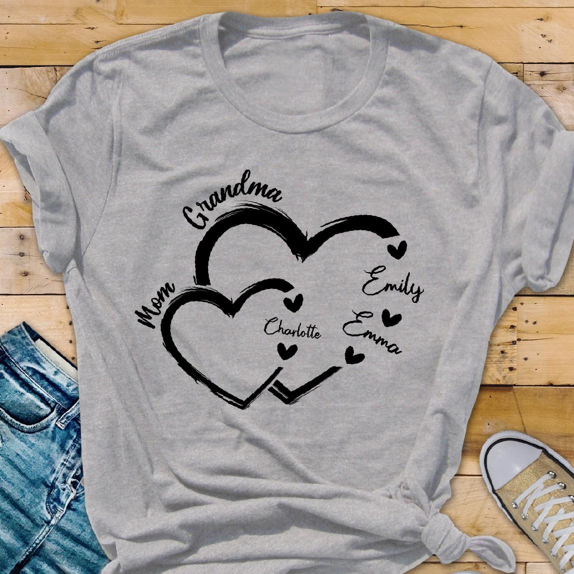 May include: Gray t-shirt with a design of two interlocking hearts. The text "Grandma" is above the hearts, and the text "Mom" is to the left of the hearts. Inside the hearts are the names "Emily", "Emma", and "Charlotte".