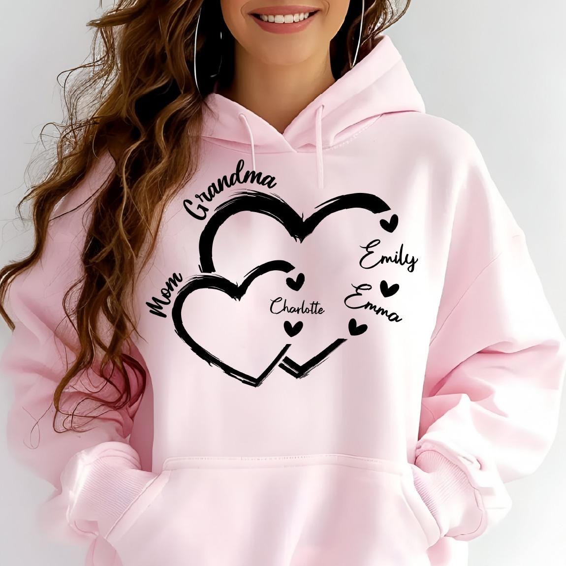 May include: Pink hoodie with a black design of two interlocking hearts. The hearts have the words "Grandma", "Mom", "Charlotte", "Emily", and "Emma" written inside them.