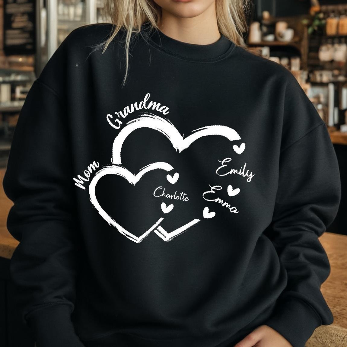May include: Black sweatshirt with a white design of two interlocking hearts. The hearts are labeled with the words "Grandma", "Mom", "Charlotte", "Emily", and "Emma".