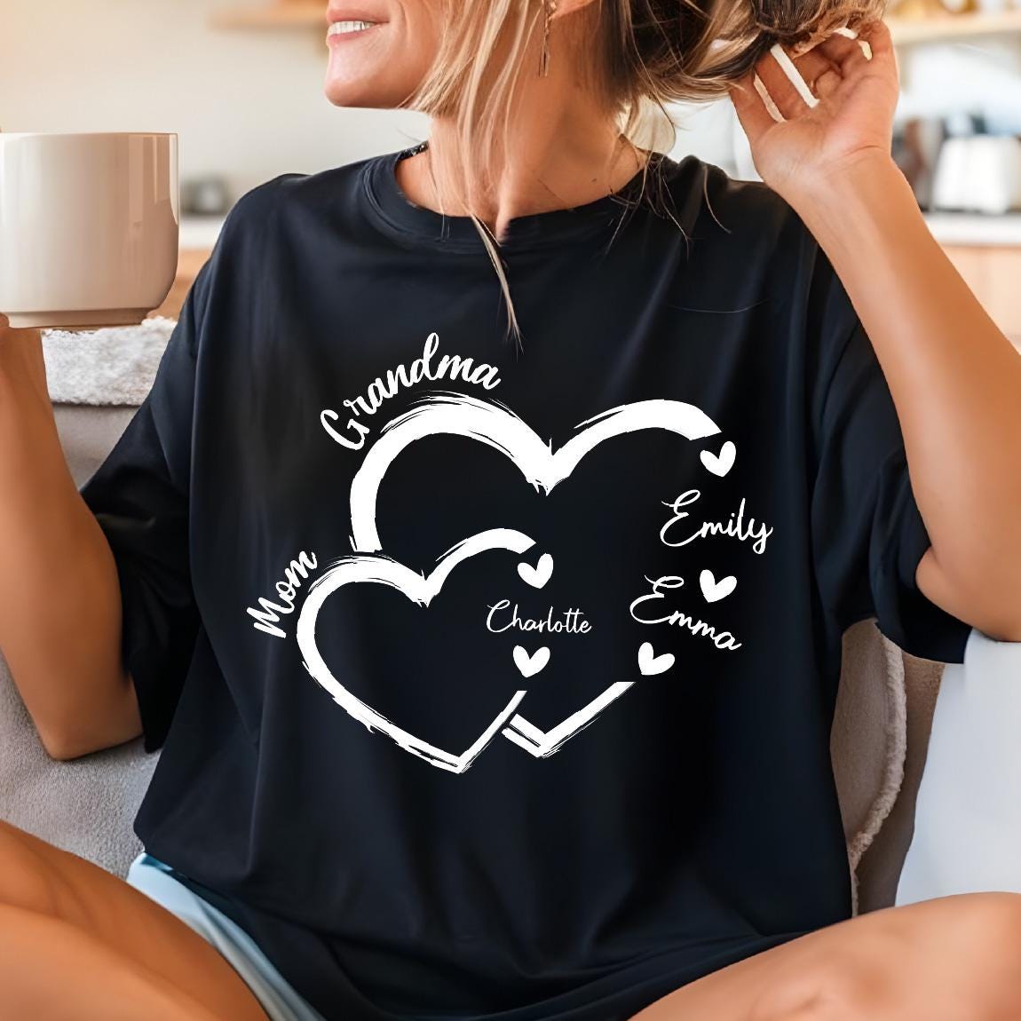 May include: Black t-shirt featuring a white heart design with the words "Grandma" and "Mom". The names "Emily", "Emma", and "Charlotte" are also displayed. The shirt is a comfortable, casual style.