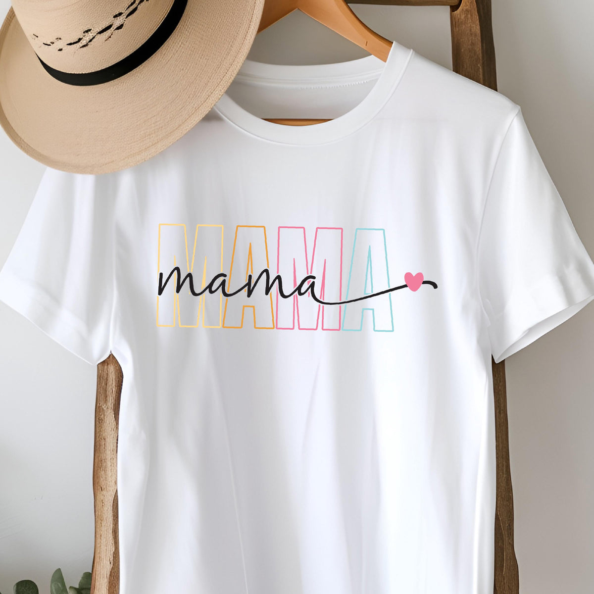 May include: White t-shirt with the word "MAMA" in rainbow colors and the word "mama" written in black script with a small pink heart.