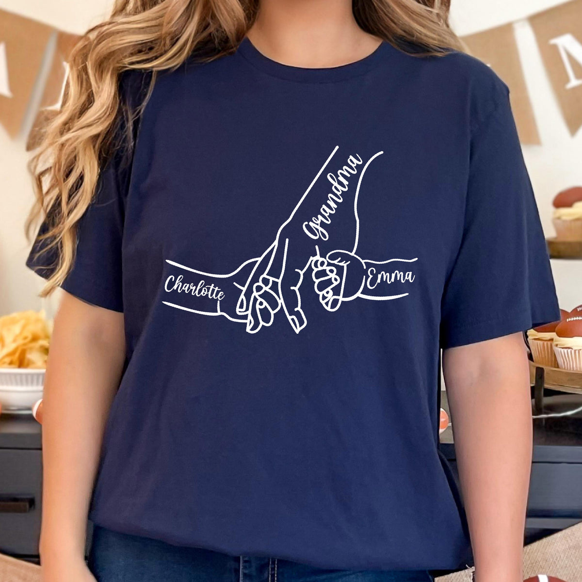 May include: Navy blue t-shirt featuring a white graphic of three hands holding each other. The word "Grandma" is written above the largest hand, with the names "Charlotte" and "Emma" on either side.