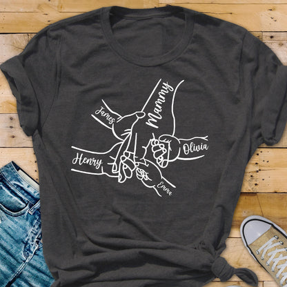 May include: Dark gray t-shirt featuring a white graphic of hands holding each other, with the names "James", "Henry", "Olivia", and "Emma" and the word "Mammy" in a script font. The shirt is made of a soft material.