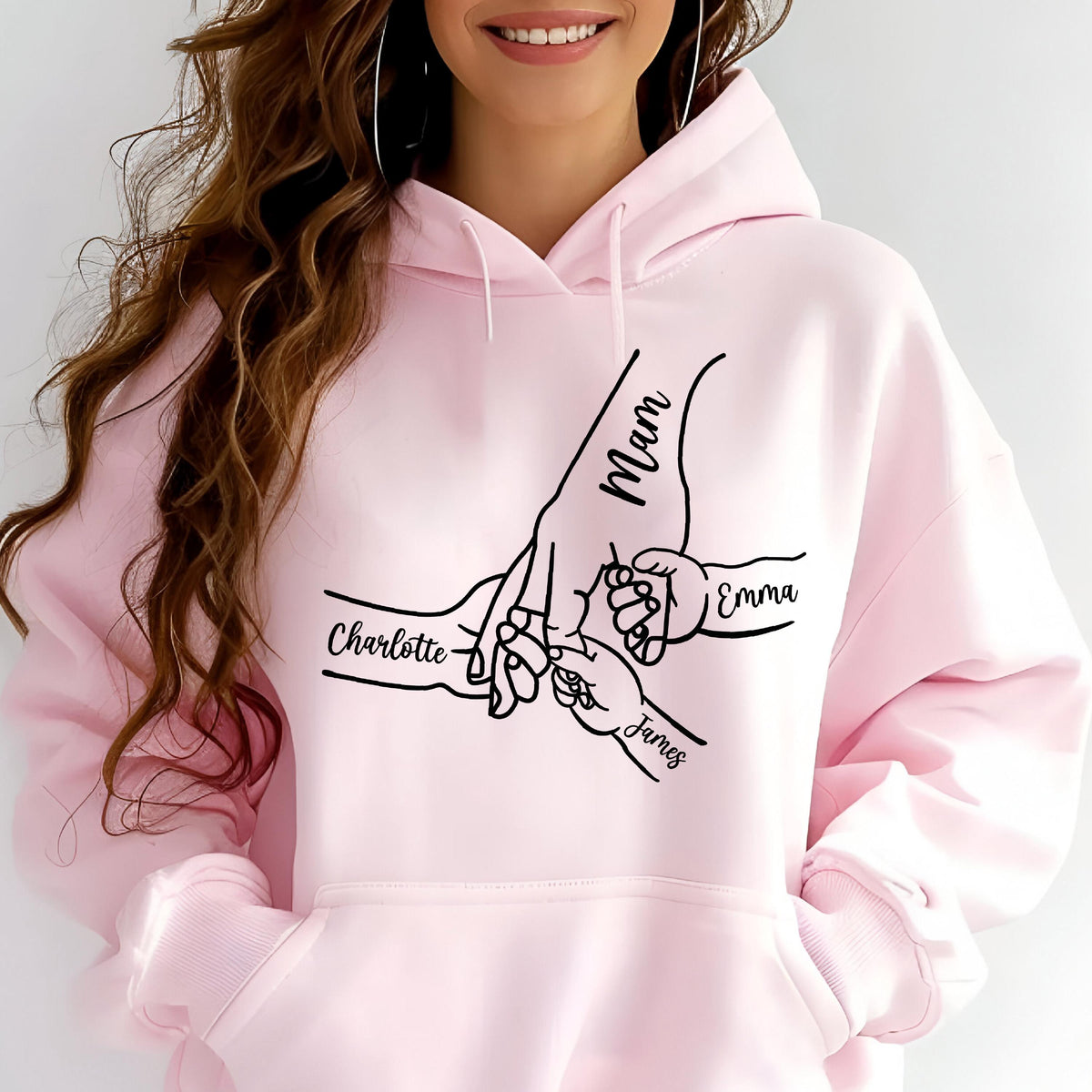 May include: Light pink hoodie with a black graphic of hands holding each other. The word "Mom" is written on the largest hand, with the names "Charlotte", "Emma", and "James" on the other hands.