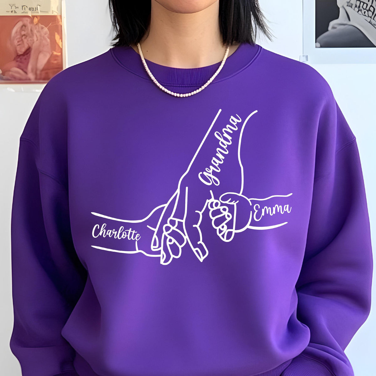 May include: A purple sweatshirt with a white graphic of hands holding each other. The names "Grandma", "Charlotte", and "Emma" are written in white script. The sweatshirt has a crew neck.
