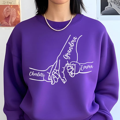 May include: A purple sweatshirt with a white graphic of hands holding each other. The names "Grandma", "Charlotte", and "Emma" are written in white script. The sweatshirt has a crew neck.