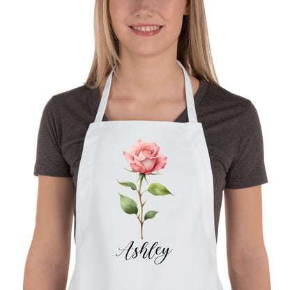 May include: White apron with a pink rose and the name Ashley printed in black cursive.