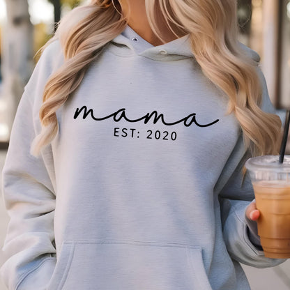 May include: A light gray hoodie with a black cursive inscription that reads "mama est: 2020".