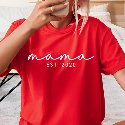 May include: A bright red short-sleeved t-shirt featuring the white text "mama" in a cursive script font, followed by the text "EST: 2020" in a clean, sans-serif typeface centered on the chest of the garment.
