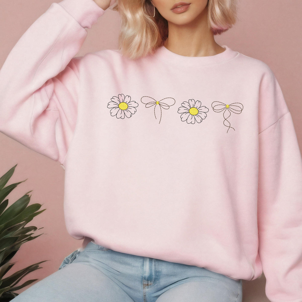 May include: A pink sweatshirt with a graphic of four daisies and bows. The daisies are white with yellow centers and the bows are black.