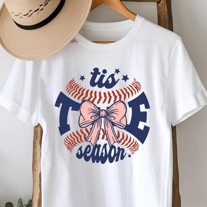 May include: White t-shirt with a blue and red baseball graphic and a pink bow. The graphic says "tis the season".