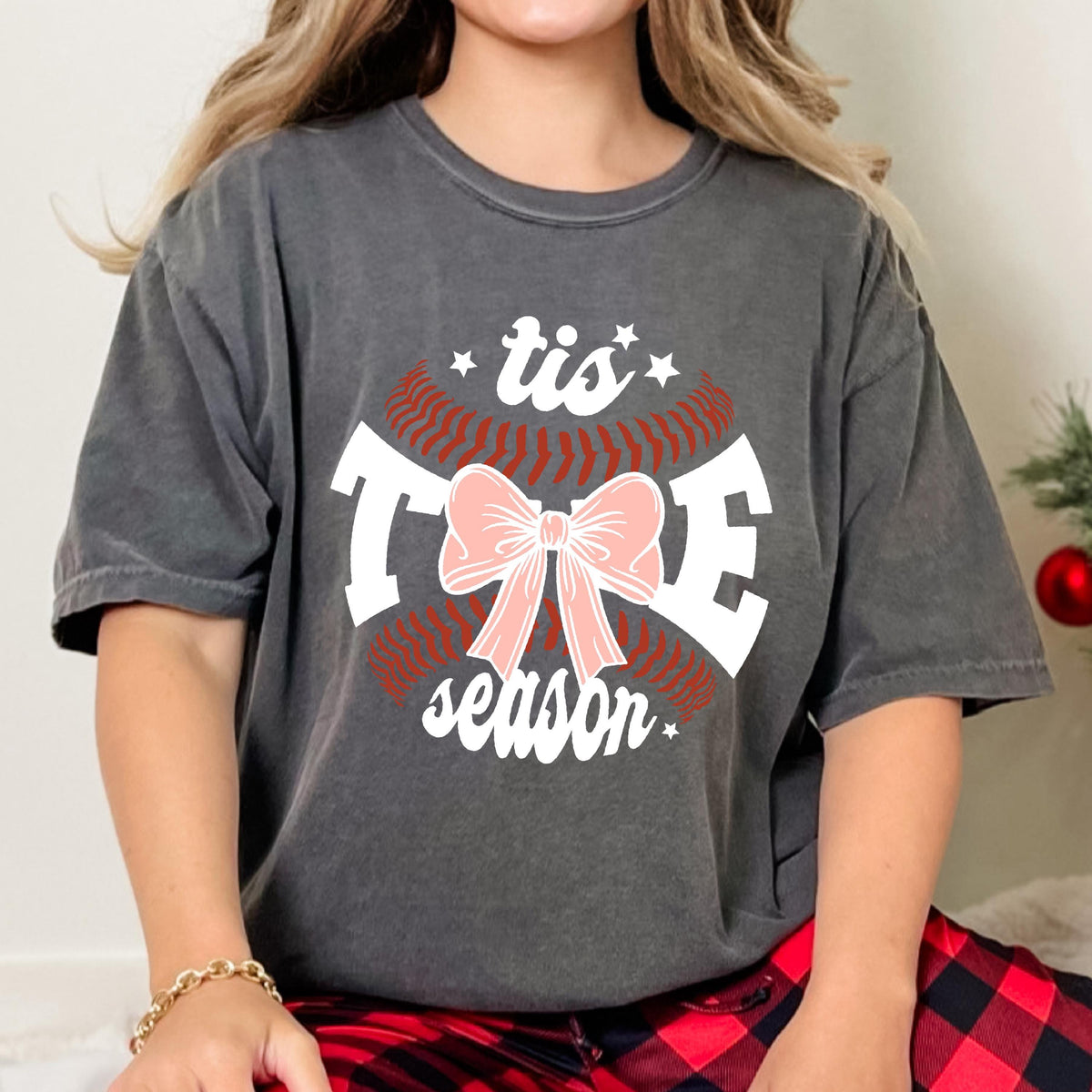 May include: A gray t-shirt with a white baseball graphic and the text "tis the season" with a pink bow in the center.