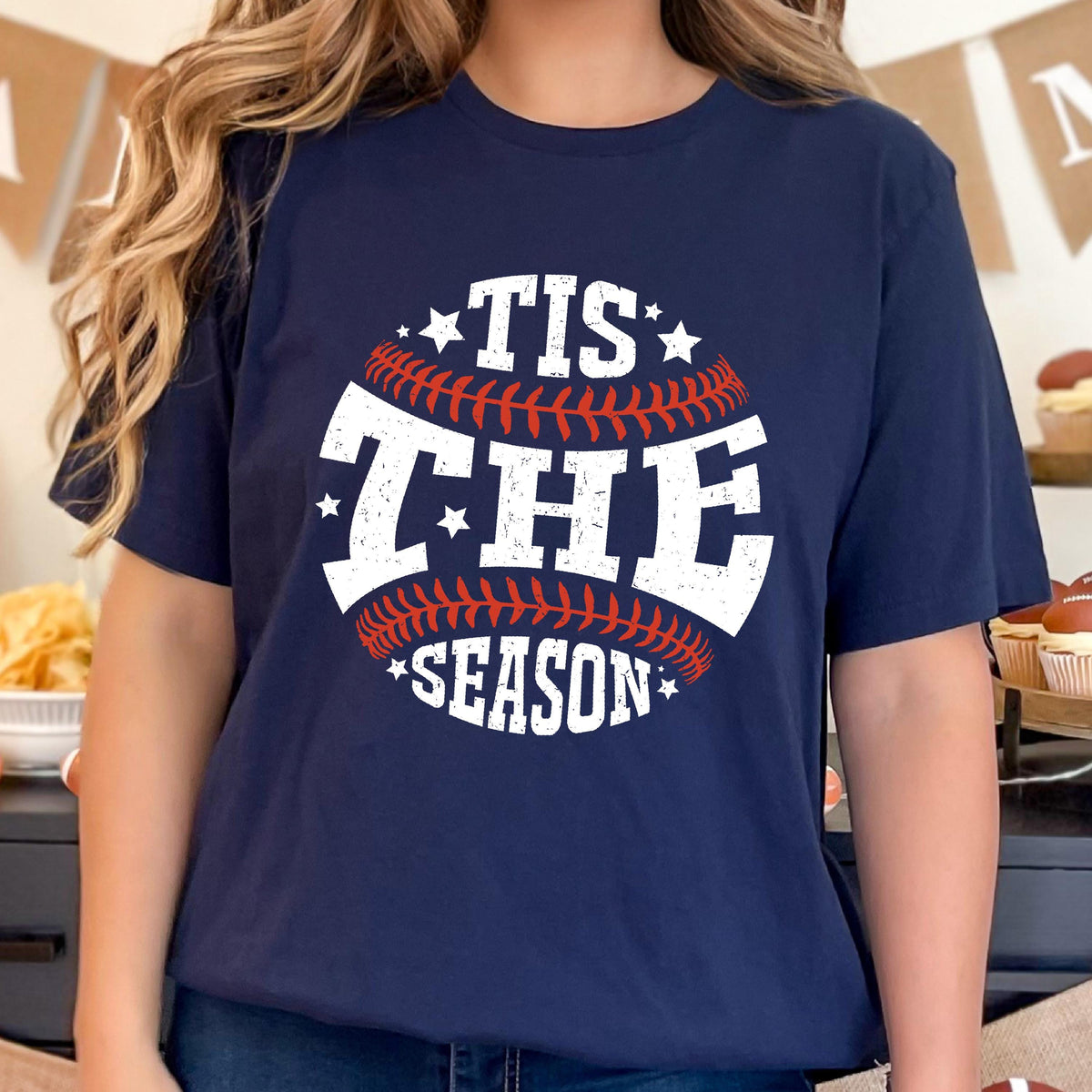 May include: A navy blue t-shirt with a white baseball graphic and the text "Tis the Season" in white with red stitching.