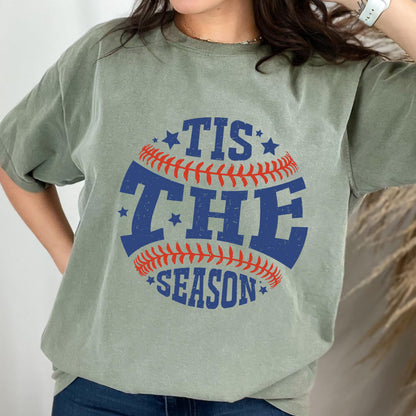 May include: A green t-shirt with a baseball graphic and the text "Tis the Season" in blue and red.