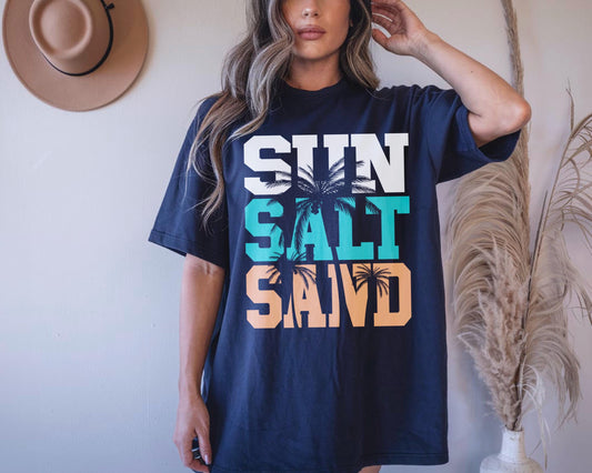 May include: A navy blue t-shirt with a graphic print of palm trees and the text "SUN SALT SAND" in white, teal, and orange.