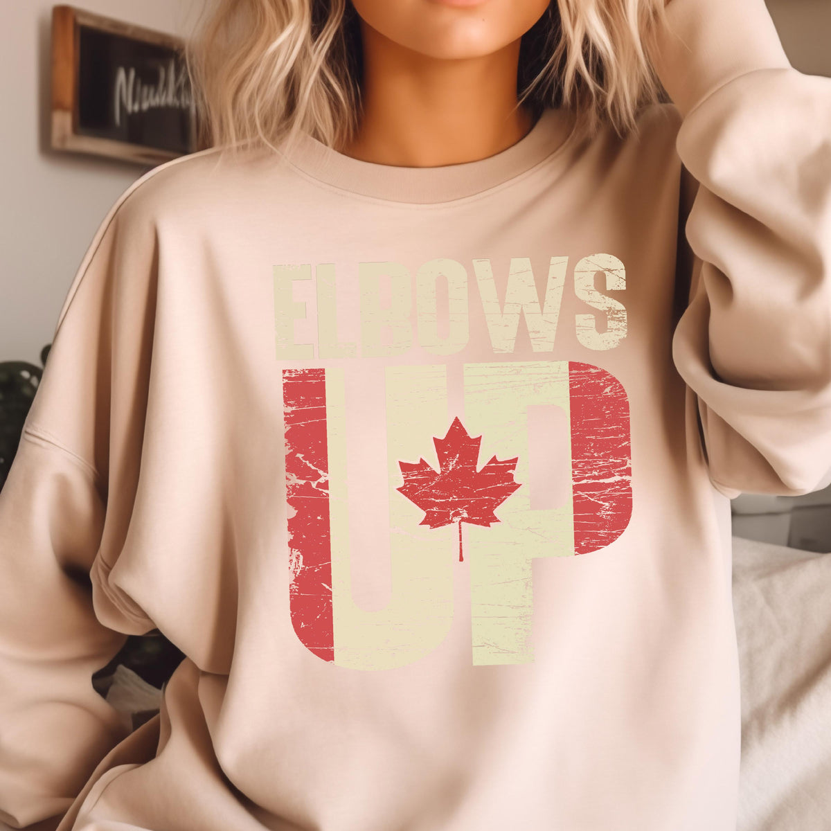 May include: A light beige sweatshirt with a distressed graphic of a Canadian flag and the text "Elbows Up".