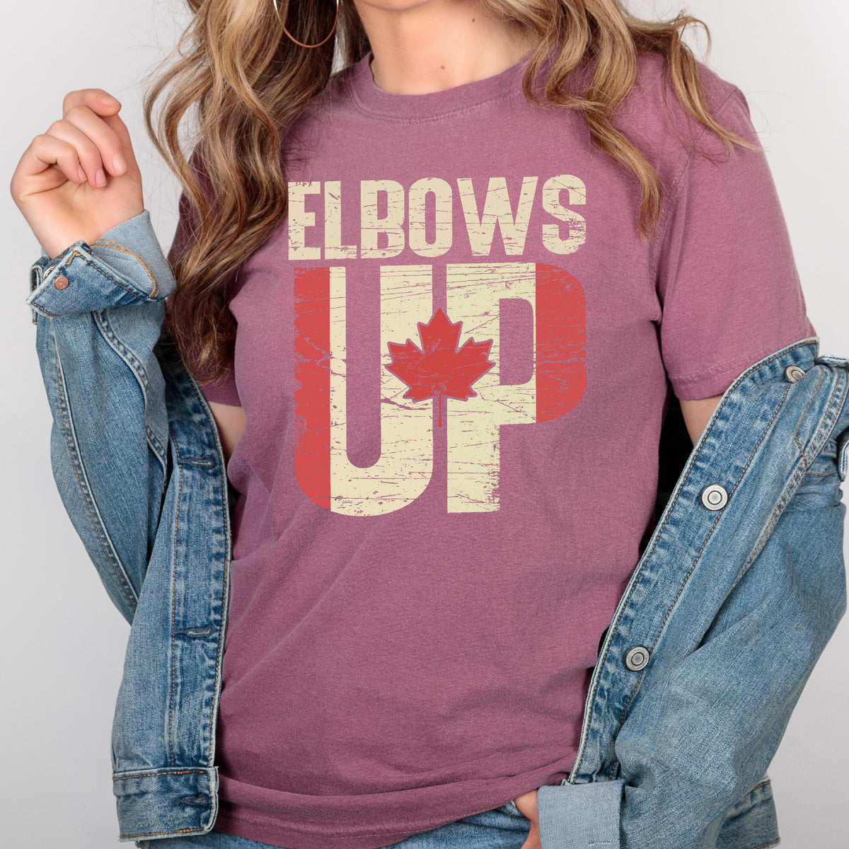 May include: A maroon t-shirt with a distressed graphic design that says "Elbows Up" with a Canadian flag design. The graphic is in white and red with a red maple leaf.