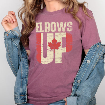 May include: A maroon t-shirt with a distressed graphic design that says "Elbows Up" with a Canadian flag design. The graphic is in white and red with a red maple leaf.