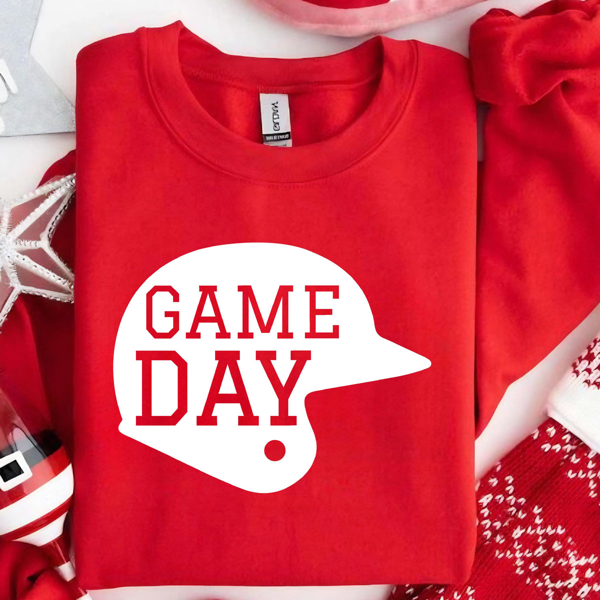May include: A bright red crewneck sweatshirt featuring a large white graphic of a baseball helmet silhouette. The text "GAME DAY" is printed in bold red capital letters inside the white helmet shape on the front of the garment.