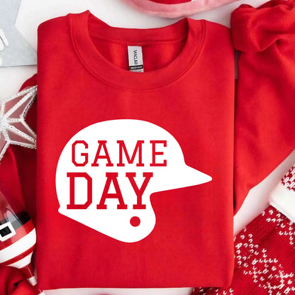 May include: A bright red crewneck sweatshirt featuring a large white graphic of a baseball helmet silhouette. The text "GAME DAY" is printed in bold red capital letters inside the white helmet shape on the front of the garment.
