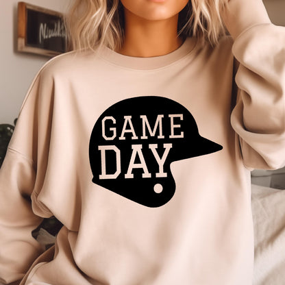 May include: A beige crewneck sweatshirt featuring a black graphic of a baseball helmet with the text GAME DAY printed in a light beige font across the center of the helmet shape. The long-sleeved garment has a simple, solid-colored design.