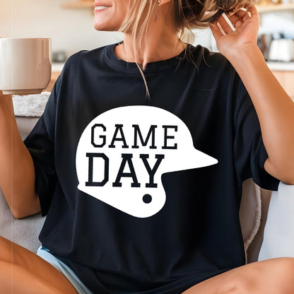 May include: A black short-sleeved t-shirt featuring a large white graphic of a baseball helmet silhouette. The text "GAME DAY" is printed in bold, black, block-style lettering inside the white helmet shape on the front of the garment.