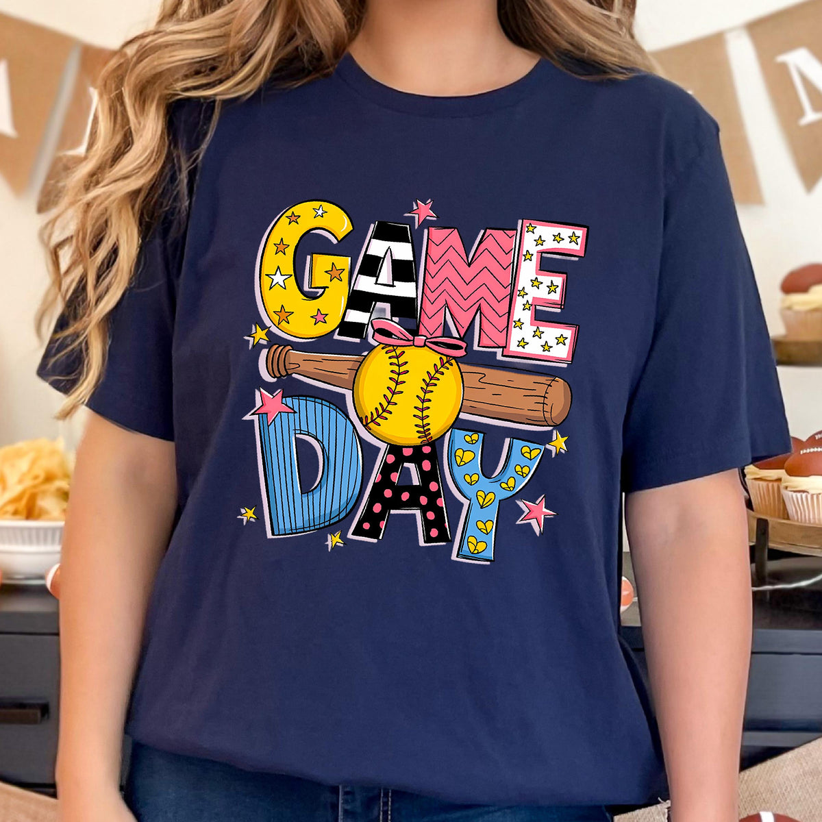 May include: A navy blue t-shirt with a colorful graphic of a baseball bat and ball with the text "GAME DAY" in a playful font.