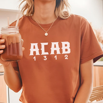 May include: A rust-colored short-sleeve t-shirt featuring the white text ACAB in a bold, stylized font with the numbers 1 3 1 2 printed directly underneath in a matching white, sans-serif typeface, centered on the chest of the garment.