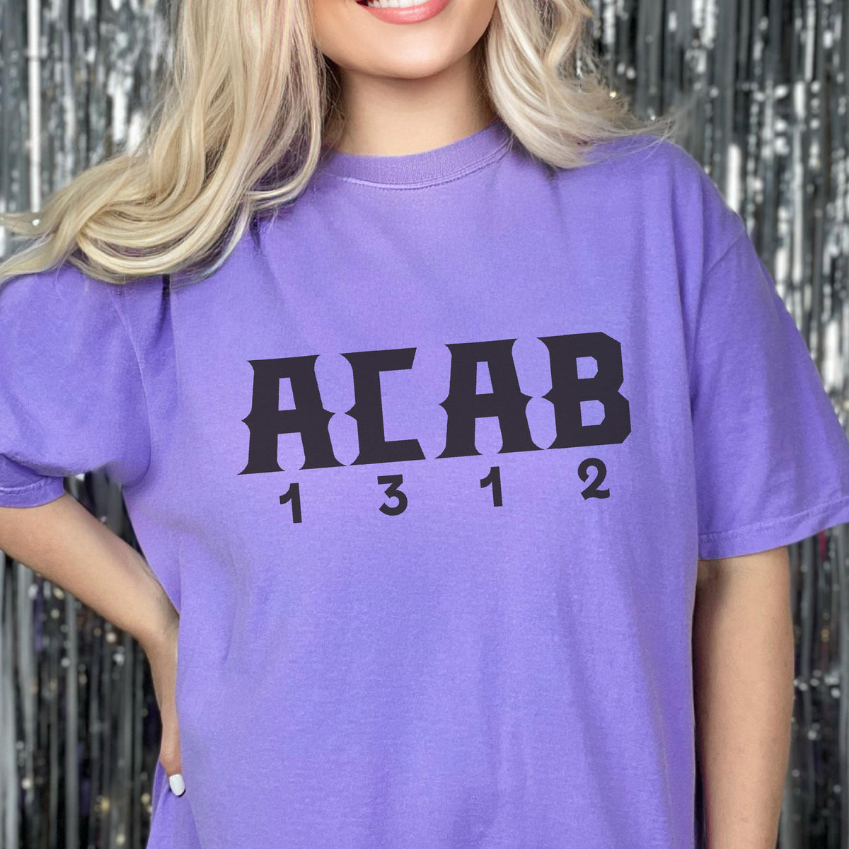 May include: A light purple short-sleeve t-shirt featuring the black text ACAB printed in a bold, blocky font across the chest. Below the letters, the numbers 1 3 1 2 are printed in a matching black font, centered horizontally on the garment.