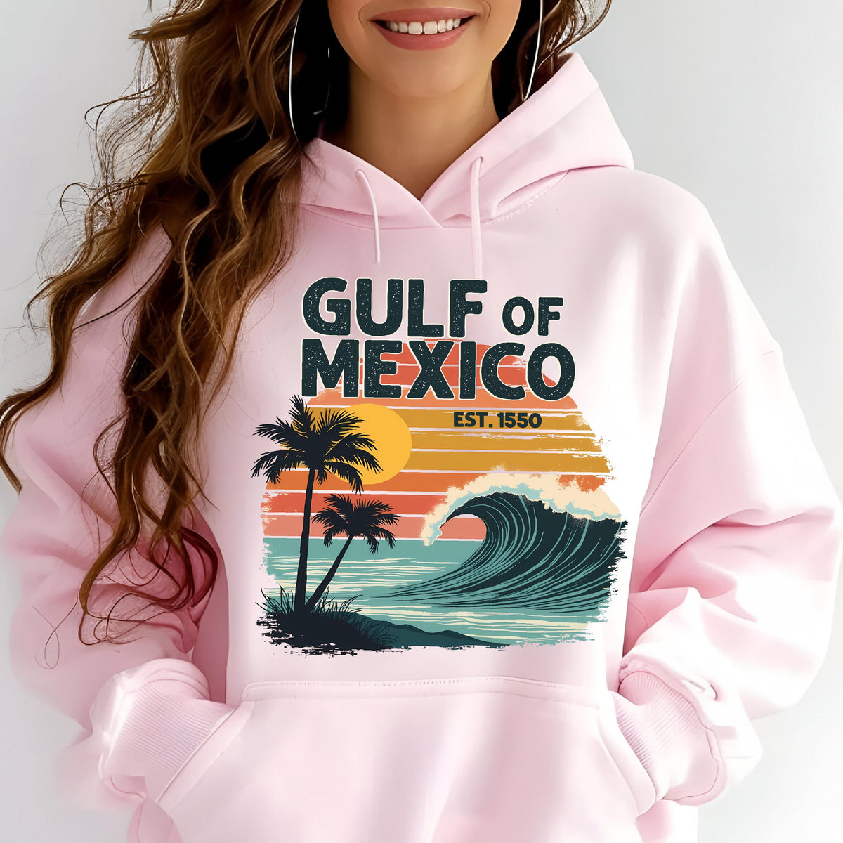 May include: Pink hoodie with a retro-style graphic design featuring a palm tree, sunset, and wave. The text on the hoodie reads "GULF OF MEXICO EST. 1550".