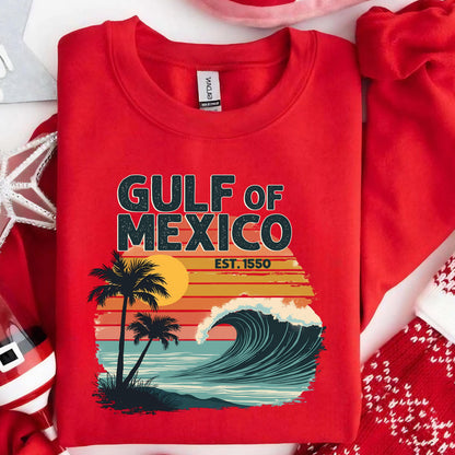 May include: Red sweatshirt with a graphic design of a sunset over the Gulf of Mexico. The graphic includes palm trees, a wave, and the text "Gulf of Mexico Est. 1550".
