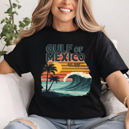 May include: Black t-shirt with a vintage-style graphic of a wave crashing on a beach with palm trees and a sunset. The text "GULF OF MEXICO EST. 1550" is printed on the shirt.