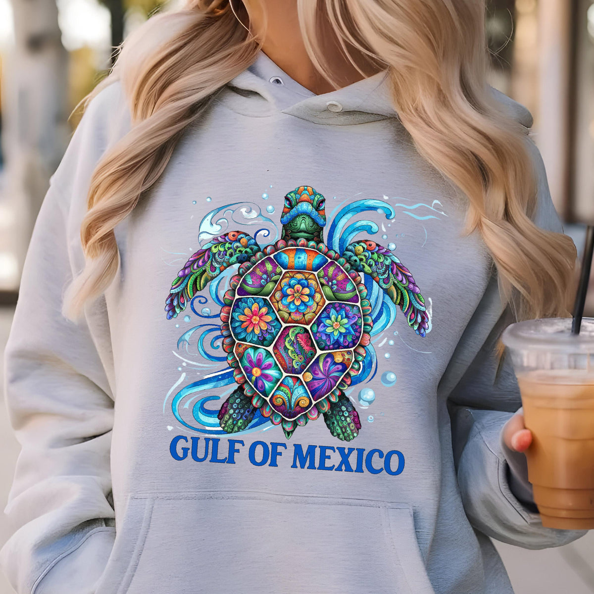 May include: A light gray hoodie featuring a colorful sea turtle design. The turtle has a patterned shell with floral accents and is surrounded by blue waves. The text "GULF OF MEXICO" is printed below the turtle.