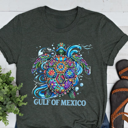 May include: A dark green t-shirt with a colorful, floral patterned sea turtle design. The turtle is surrounded by blue waves and bubbles. The text "GULF OF MEXICO" is printed below the turtle.
