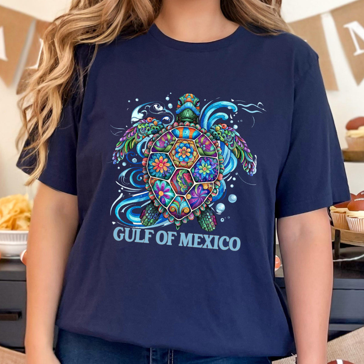 May include: A navy blue t-shirt with a colorful, patterned sea turtle design. The turtle is surrounded by blue waves and bubbles. The text "GULF OF MEXICO" is printed below the turtle.