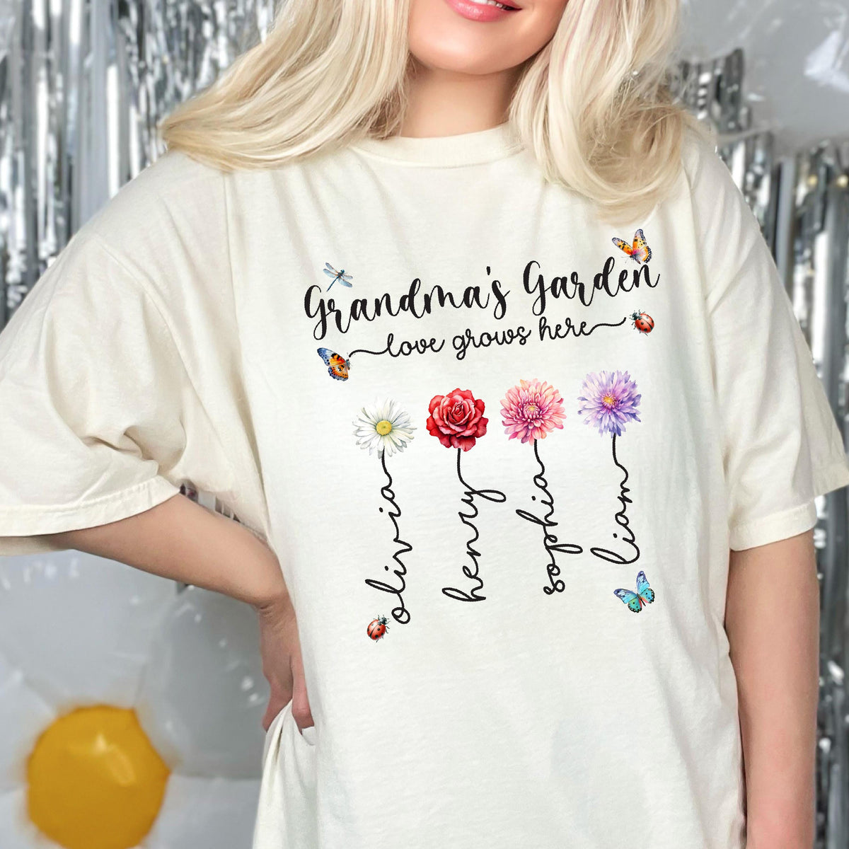 May include: A white t-shirt with the text "Grandma's Garden - love grows here" and four flowers with names Olivia, Henry, Sophia, and Liam written underneath.