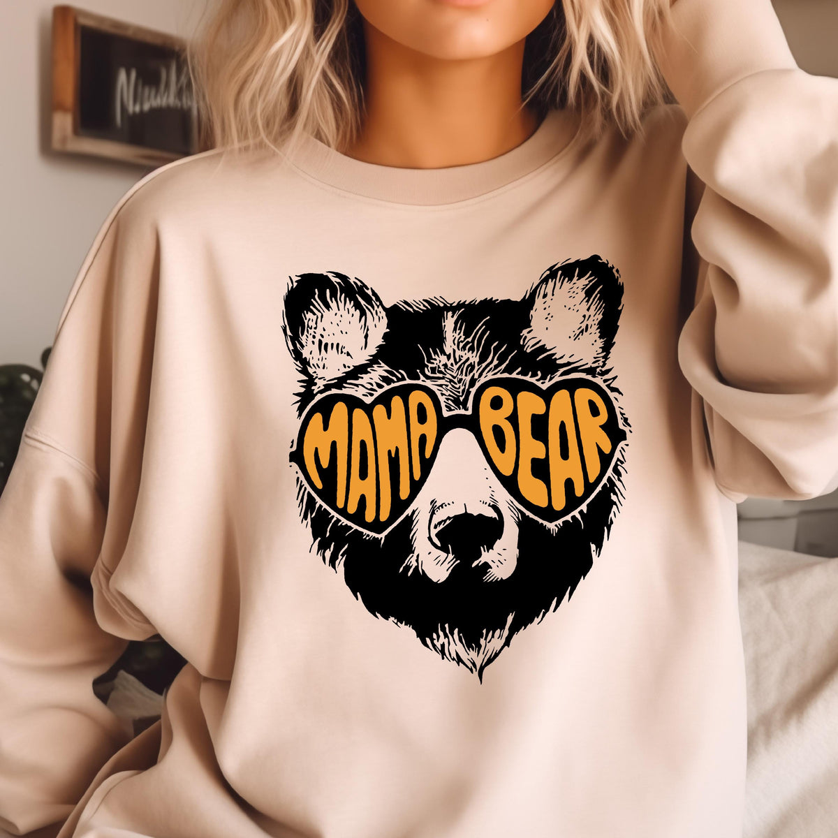 May include: A beige sweatshirt with a black bear wearing heart-shaped sunglasses that say "Mama Bear" in orange letters.